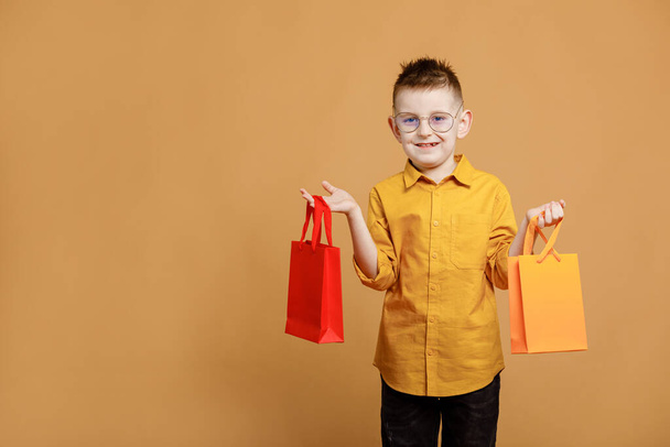 Shopping on black friday. Little boy holding shopping bags on yellow background. Shopper with many colored paper bags. Holidays sales and discounts. Cyber monday. High quality photo. - Foto, afbeelding