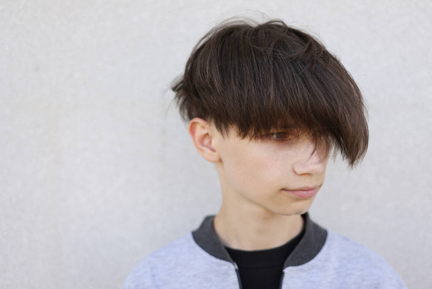 Jóképű fiatalember elegáns frizurával. Portré tini fiú ifjúsági frizura áll szürke háttér - Fotó, kép