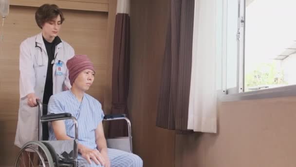 Egyenruhás fiatal kaukázusi nő terápia orvos tolja tolószék férfi beteg ablakhoz, támogatja és motiválja talpra daganatos betegség után kemoterápiás kezelés kórházi fekvőbeteg szobában. - Felvétel, videó