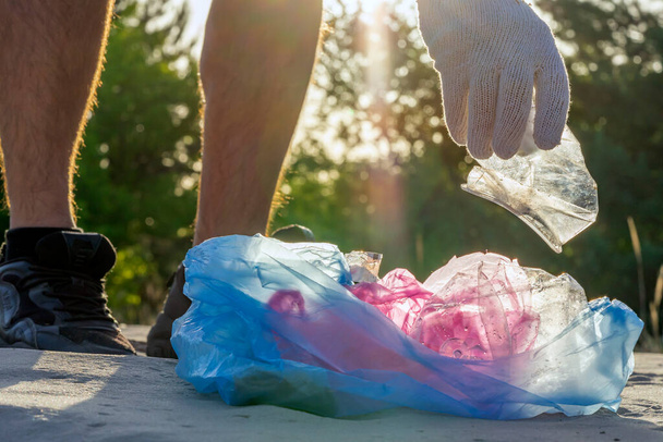 Plastic pollution in the environmental problem of the world. A hand in a white glove puts garbage in a plastic bag. Removal and cleaning of garbage from contaminated territories - Valokuva, kuva