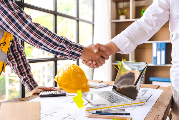 Mimarlar ve mühendisler, inşaat işçileri, başarılı bir iş birliği konsepti ofis inşaatı üzerinde anlaşma sağlandıktan sonra takım olarak çalışırken el sıkışıyorlar.. - Fotoğraf, Görsel