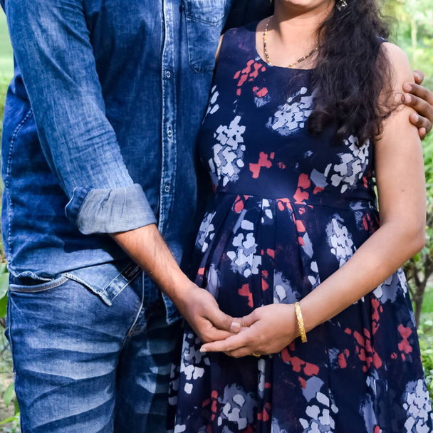 乳児撮影のためにポーズをとるインドのカップル。二人は緑の草の芝生の上でポーズをとっている女性はインドのニューデリーにあるロディ・ガーデンで赤ん坊のバンプを落下させている - 写真・画像
