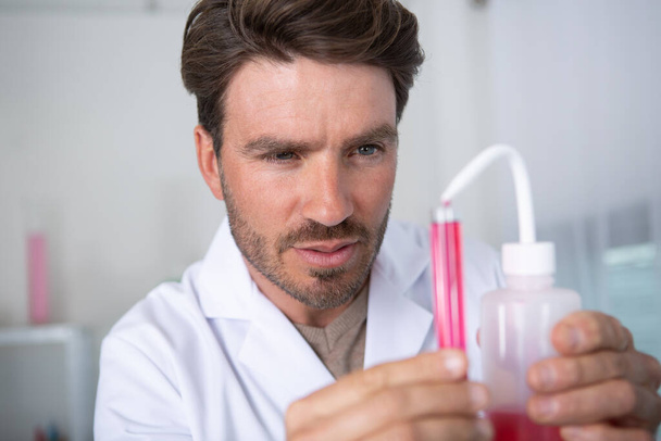 male scientist pouring red liquid from beaker into test tube - 写真・画像