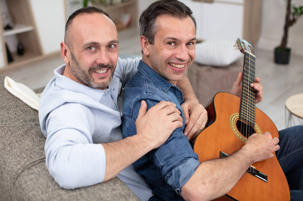 gay couple with guitar sitting on sofa at home - Foto, imagen