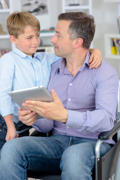 dad in a wheelchair with his son using a tablet - Photo, Image