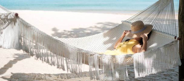 Happy Woman Traveler χαλαρώνει σε μια αιώρα στην παραλία του παραδείσου. Γυναίκα τουρίστρια με κίτρινο φόρεμα ξεκουράζεται κοντά στην τροπική θάλασσα. διακοπές, ταξίδια, καλοκαίρι, Wanderlust και έννοια των διακοπών - Φωτογραφία, εικόνα