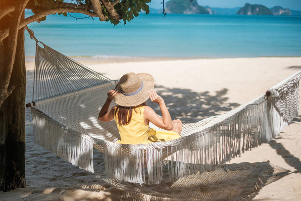 Happy Woman Traveler отдыхает в гамаке на пляже Paradise. Женщина туристка в желтом платье отдыхает у тропического моря. Понятие отпуска, путешествия, лета и отпуска - Фото, изображение