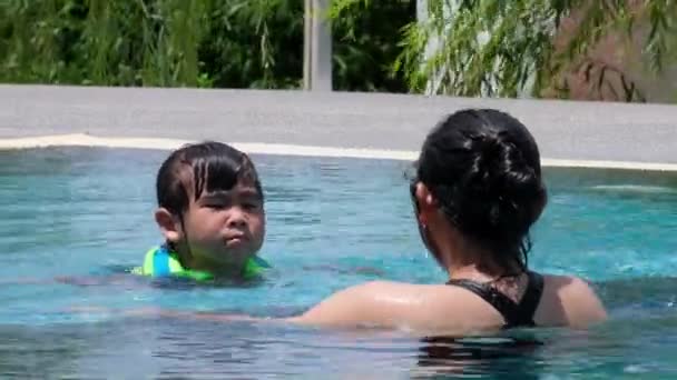 Can yeleği giymiş küçük bir kız derin havuzda yüzmekten korkar. Anne kızına havuzda yüzmeyi öğretiyor. Mutlu aile, annesi ve kızı yüzme havuzunda oynuyorlar. Yaz yaşam tarzı konsepti. - Video, Çekim