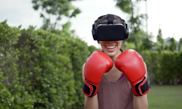 Boks yapmak için VR kulaklık takan genç bir kadın, simülasyon dünyasında boks yapmak için aerobik eğitimi alan bir kadın.. - Fotoğraf, Görsel