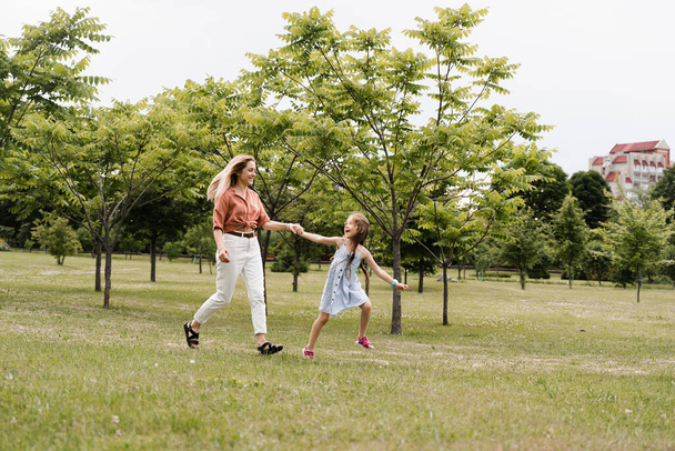 Mamá y su hija corren por el parque y se divierten. Valores y tradiciones familiares. Feliz infancia de un niño. Madre juega con su hija - Foto, Imagen