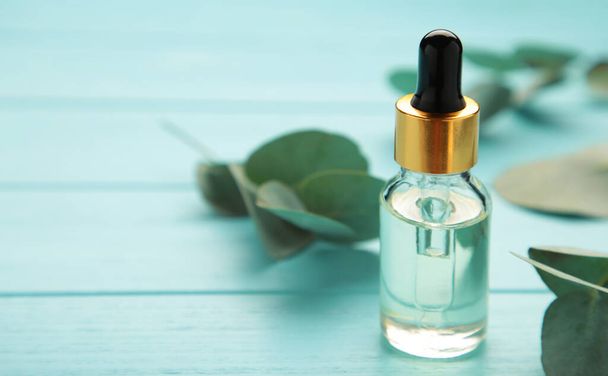 Eucalyptus Essential Oil in bottle with green leaves on blue background. Top view - Foto, Imagen