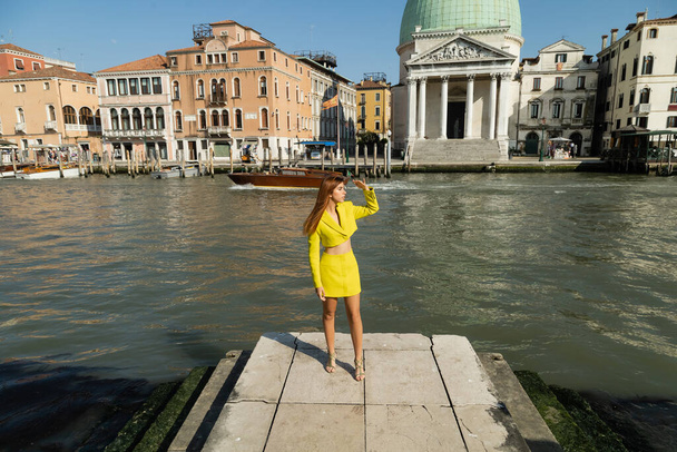 Frau in gelber Kleidung blickt auf Pier in der Nähe des Canal Grande in Venedig weg - Foto, Bild