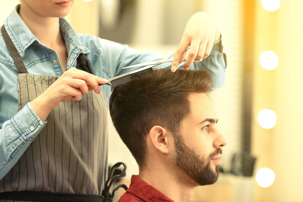 Barber making stylish haircut with professional scissors in beauty salon - Fotó, kép