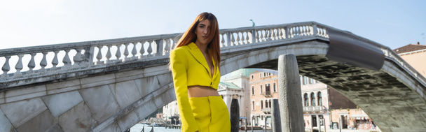 redhead woman in yellow trendy suit posing near venetian bridge on background, banner - Photo, Image