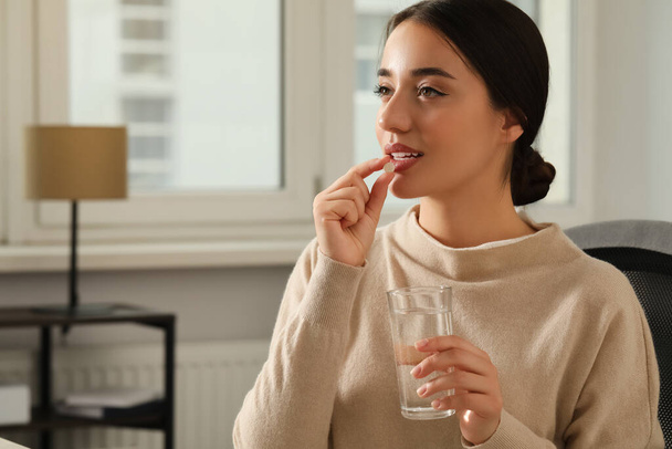 Young woman with glass of water taking dietary supplement pill indoors, space for text - Foto, immagini