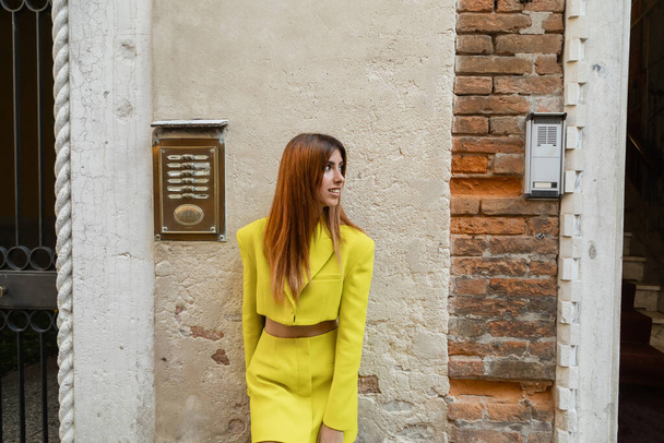 ruda kobieta w żółtym garniturze uśmiecha się i patrzy w pobliżu budynku w Wenecji - Zdjęcie, obraz