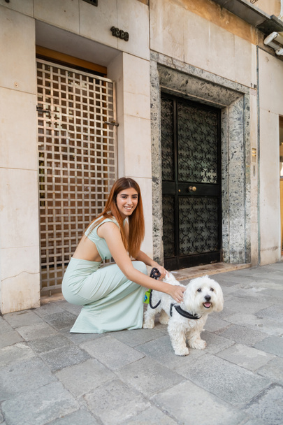 Elegante Frau lächelt, während sie weißen Hund auf der Straße in Venedig streichelt - Foto, Bild