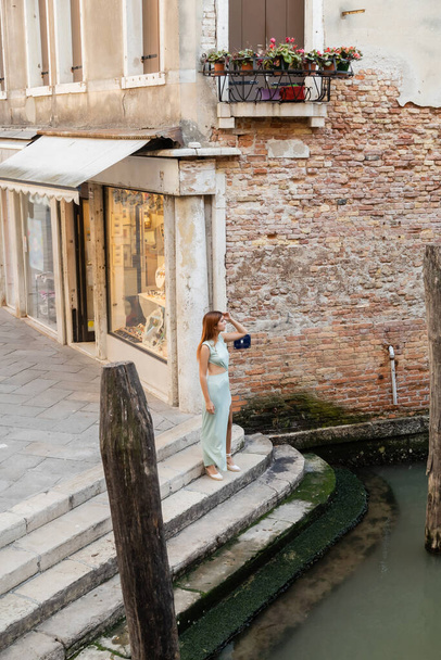 full length of elegant woman standing on stairs near city canal in Venice - Photo, Image