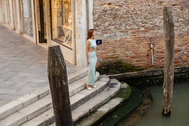 volledige lengte van elegante vrouw op trappen in de buurt van water en houten palen in Venetië - Foto, afbeelding