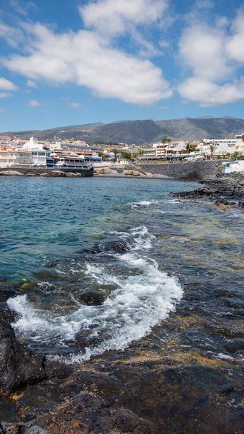 La Caleta, Costa Adeje, Teneryfa, Wyspy Kanaryjskie, Hiszpania - 5 maja 2019: widok na małą malowniczą wioskę od poziomu oceanu w górę w kierunku budynków mieszkalnych, restauracji i promenady - Zdjęcie, obraz