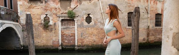 Venedik 'teki ortaçağ binasına bakan zarif elbiseli kızıl saçlı kadının yan görüntüsü. - Fotoğraf, Görsel