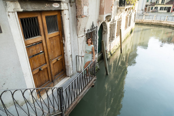žena v elegantních šatech stojící na balkóně středověké budovy nad kanálem v Benátkách - Fotografie, Obrázek