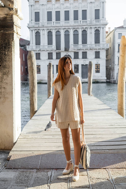 full length of woman with striped bag looking away near wooden pier in Venice - Φωτογραφία, εικόνα