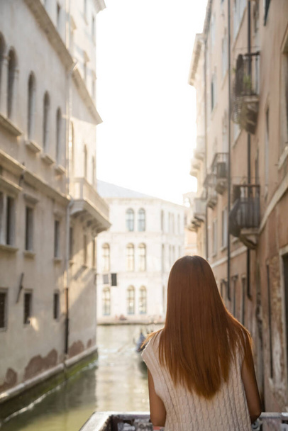 задний вид женщины с рыжими волосами возле размытых средневековых зданий в Венеции - Фото, изображение