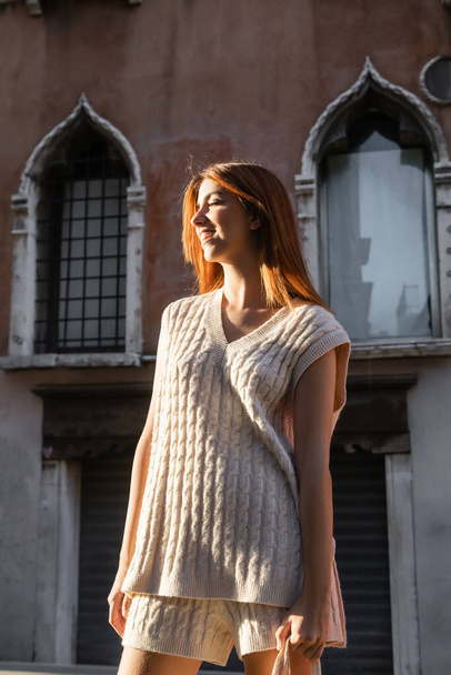 young woman in sleeveless jumper smiling near blurred building in Venice - 写真・画像