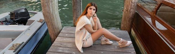 high angle view of young woman sitting on wooden pier near motor boats in Venice, banner - Photo, Image