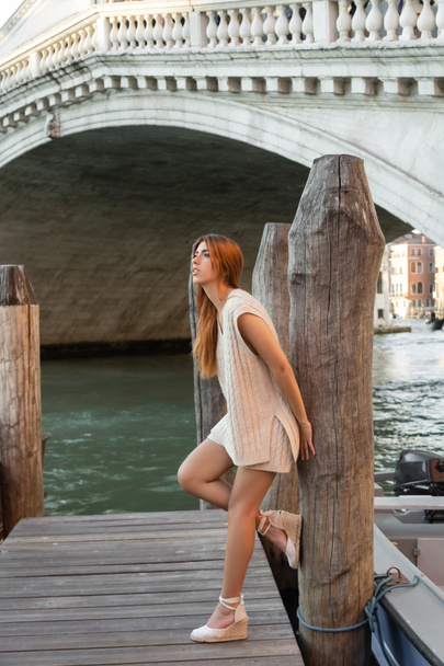 stylish woman in wedge sandals leaning on wooden piling near bridge over Grand Canal in Venice - Valokuva, kuva
