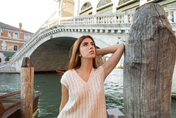fiatal nő néz félre közel fa cölöp és Rialto híd a háttérben Velencében - Fotó, kép
