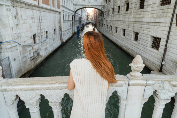 back view of redhead woman standing on bridge near medieval prison in Venice - Foto, imagen