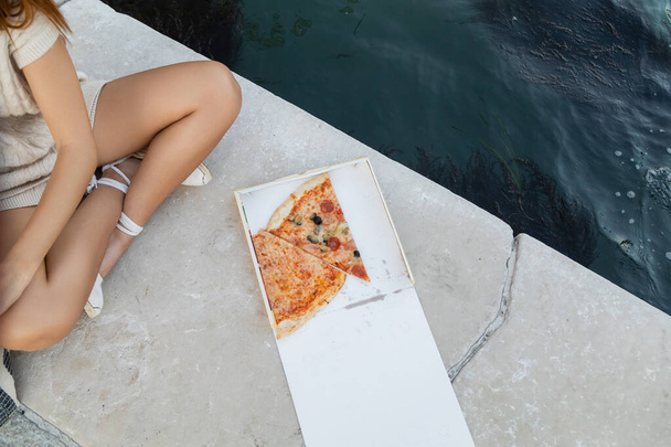 top view of tasty pizza near cropped woman sitting with crossed legs near water in Venice - Fotoğraf, Görsel
