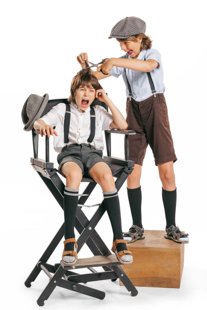 At barber shop. Two school age boys, stylish kids wearing retro clothes, shorts with suspenders isolated over white background. Concept of childhood, vintage summer fashion style. Copy space for ad - 写真・画像