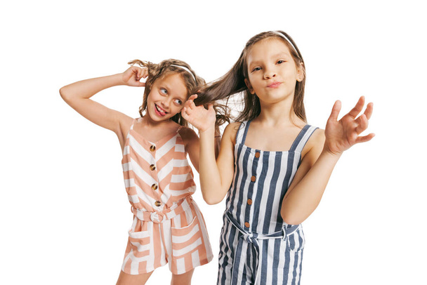 Having fun. Portrait of two cheerful girls in retro style summer outfit isolated on white background. Concept of kids emotions, facial expression, beauty, childhood. Copy space for ad - Foto, Bild
