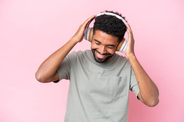 Молодой бразилец на розовом фоне слушает музыку - Фото, изображение