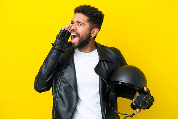 Молодой бразилец с мотоциклетным шлемом на желтом фоне кричит с широко раскрытым ртом в сторону - Фото, изображение