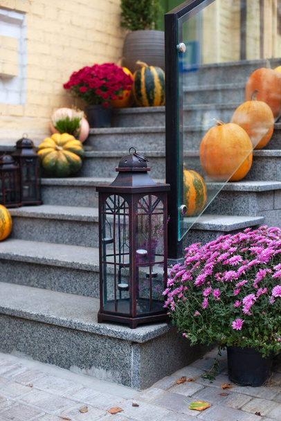 Лестница украшена для осенних праздников, осенних цветов и тыкв. Уютное крыльцо дома с винтажными фонарями осенью. Дизайн на Хэллоуин с желтыми кедами и ленточками - Фото, изображение
