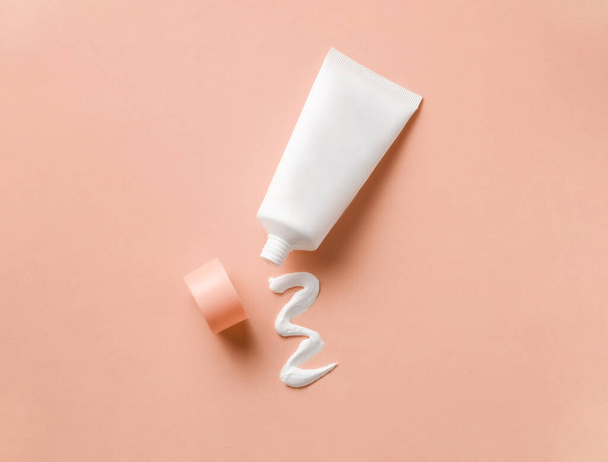 Clean label facial body cream tube with open cap and product squeezed cream texture on flesh color background. Top view, copy space - Photo, Image