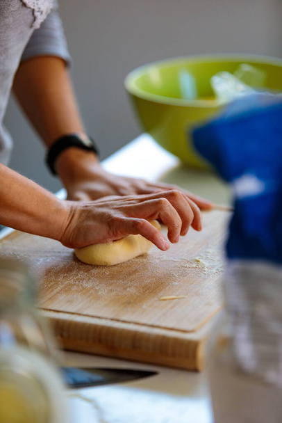 A vertical shot of hands stretching dough on a wooden board in the kitchen - Foto, imagen