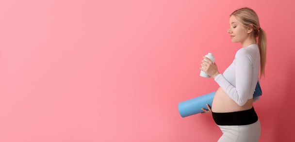 Nuori raskaana oleva nainen, jolla on joogamatto ja pullo vettä vaaleanpunaisella taustalla ja tilaa tekstille - Valokuva, kuva
