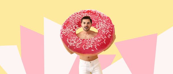 Handsome man with big tasty donut on color background - Foto, afbeelding