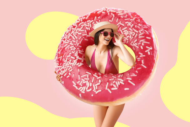 Schöne junge Frau im Badeanzug und mit großen leckeren Donut auf Farbhintergrund - Foto, Bild