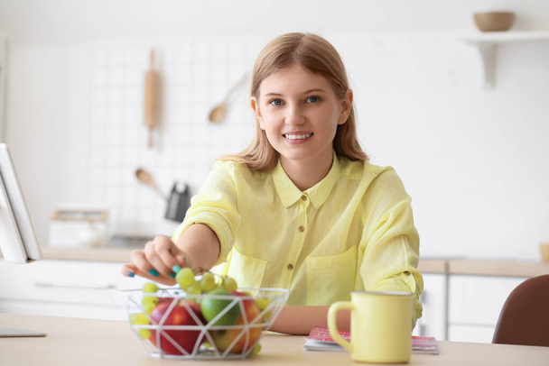 Adolescente menina tomando uva de cesta na mesa na cozinha - Foto, Imagem