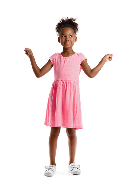 Маленькая афроамериканка в розовом платье указывает на что-то на белом фоне - Фото, изображение