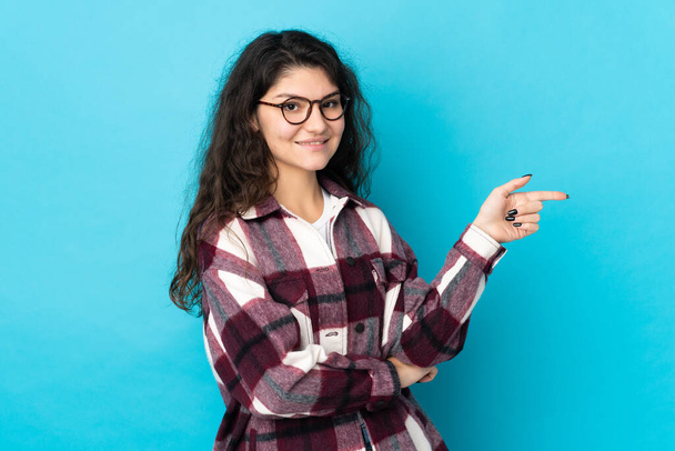 Teenager Russian girl isolated on blue background pointing finger to the side - Foto, Imagen