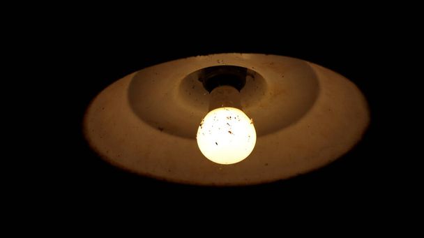 A closeup of a ceiling light shining with the lightbulb covered in dust and spider webs - Foto, immagini