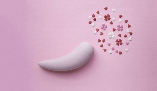 Рожева вакуумна стимуляторна іграшка для дорослих лежить на рожевому тлі, поруч з декоративними серцями імітує оргазм. Концептуальне фото
. - Фото, зображення