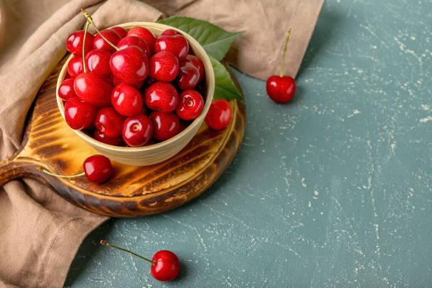 Wooden board with bowl of sweet cherries on color background - Photo, Image